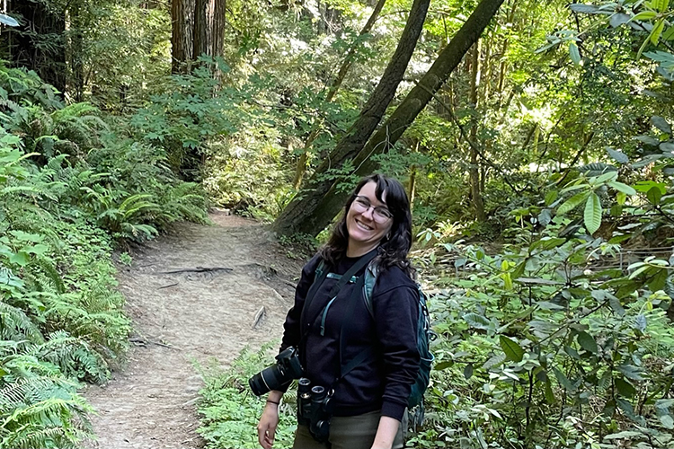 Artist Lora Roame looks at the camera and smiles as she walks along a hiking trail.