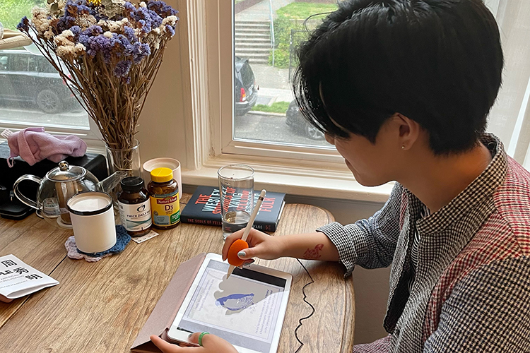 Artist Ning Wang works on digital artwork on an iPad on a table near a window.