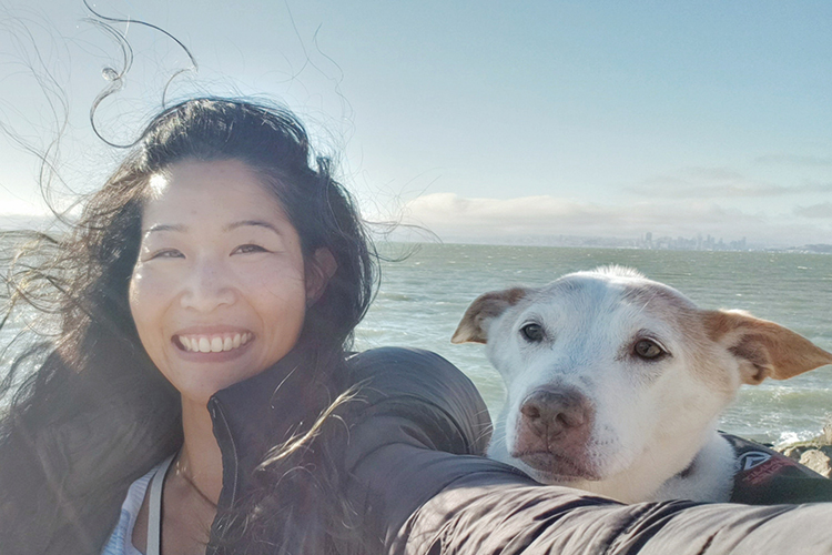 Berkeley alumna Sandy Lwi took this selfie with her dog near the Berkeley Marina. The wind is blowing her hair. She and her dog are looking straight at the camera.
