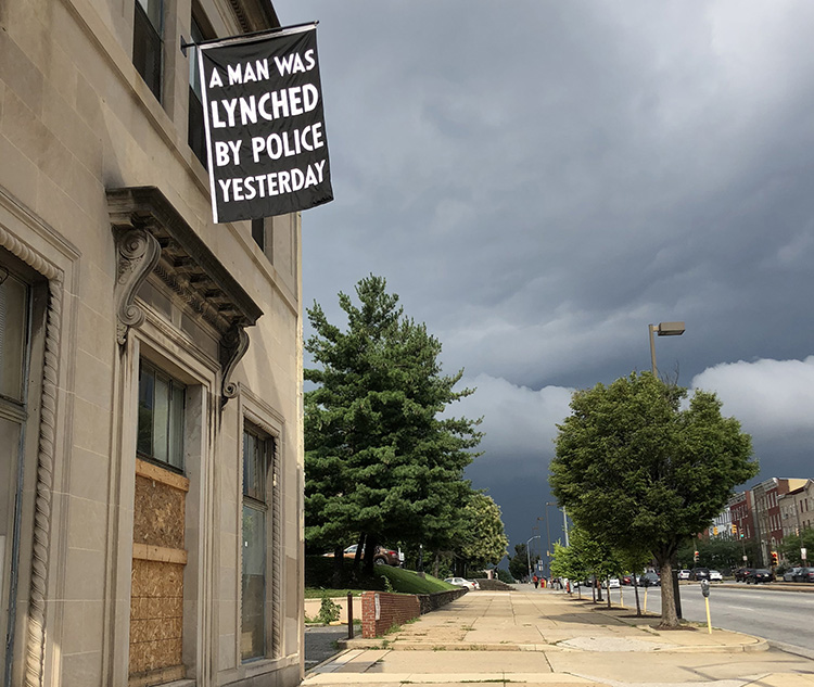 Flag hanging from building that says "A man was lynched by police yesterday."