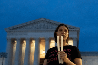 a solemn protester with two candles stands before the US Supreme Court building as darkness falls
