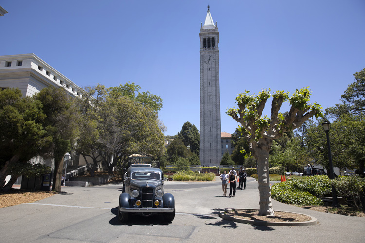old cars and people walk on a sunny day on campus near sather tower