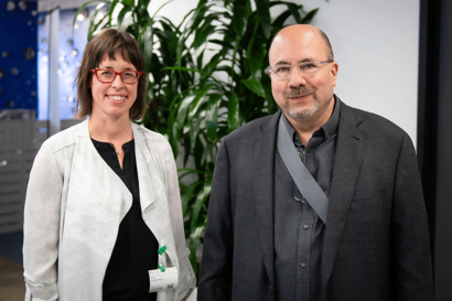 A photo of Ann Cleaveland and Craig Newmark standing next to each other in front of a large plant.