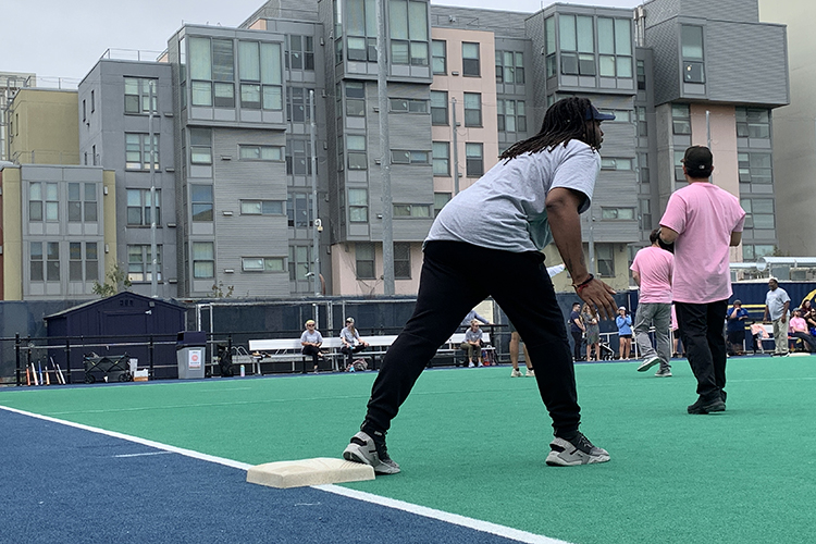 Jonathon Walker, a new campus employee, plays on the UHS softball team. In this photo, he's wearing the team's grey T-shirt and has one foot on base.