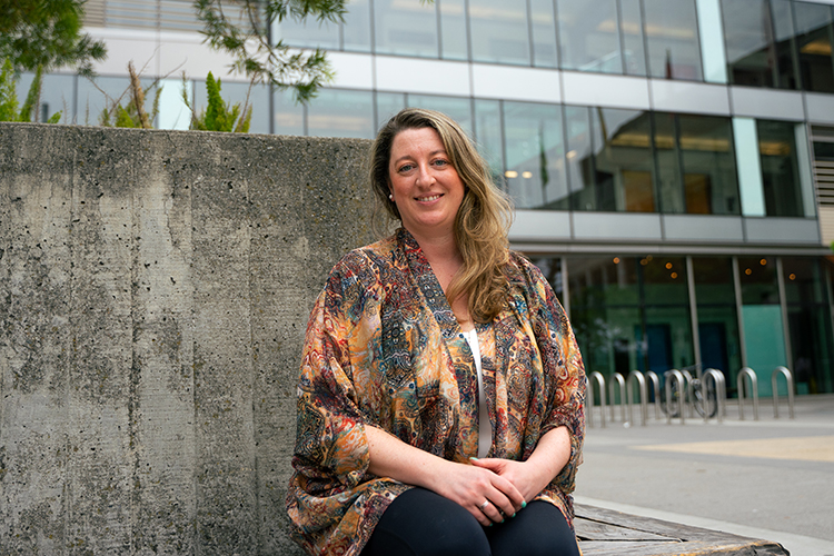 Sarah Gaugler, an ERSO contracts and grants supervisor, poses, seated, in front of a campus building.