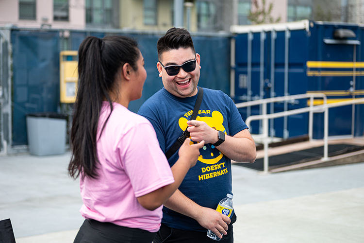 Two members of the Student Affairs Summer Softball League smile and talk together, standing close, at Underhill Field.