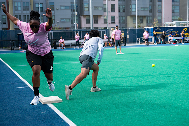 In a pink Residential Life team T-shirt, Edtivia Ruther runs to first base during a Student Affairs Summer Softball League game in summer 2022.