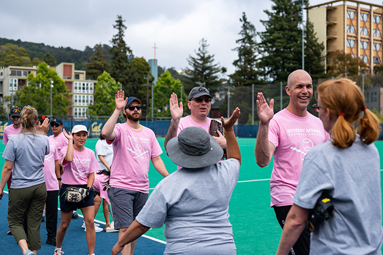 Softball league players, some of them smiling, high-five each other after a game between University Health Services and Residential Life staffers.