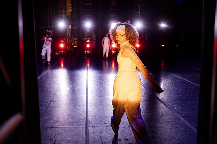 a dancer looks over her shoulder on a dark stage with bright lights
