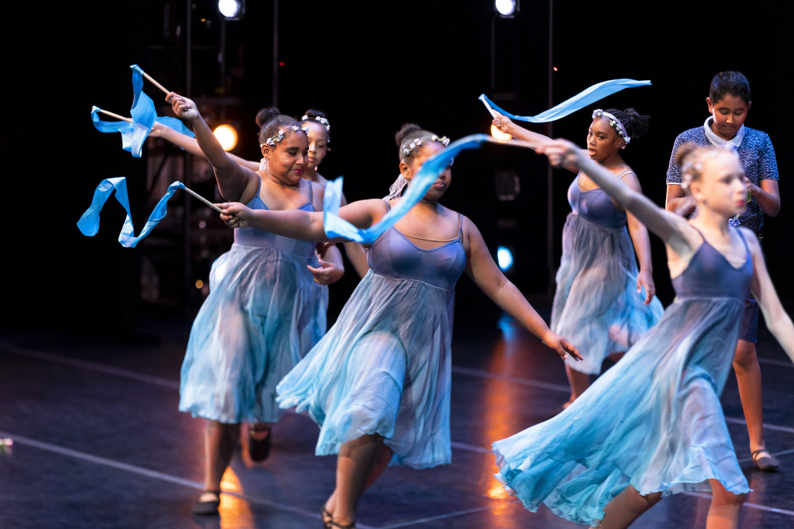 dancers in blue dresses dance with blue ribbons on stage