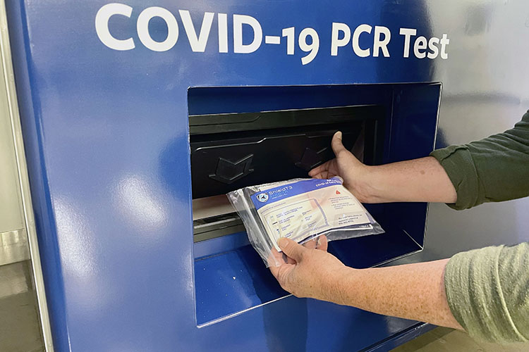 A close-up shot of someone's hands taking a free COVID-19 PCR test out of a vending machine at the MLK Jr. Student Union.