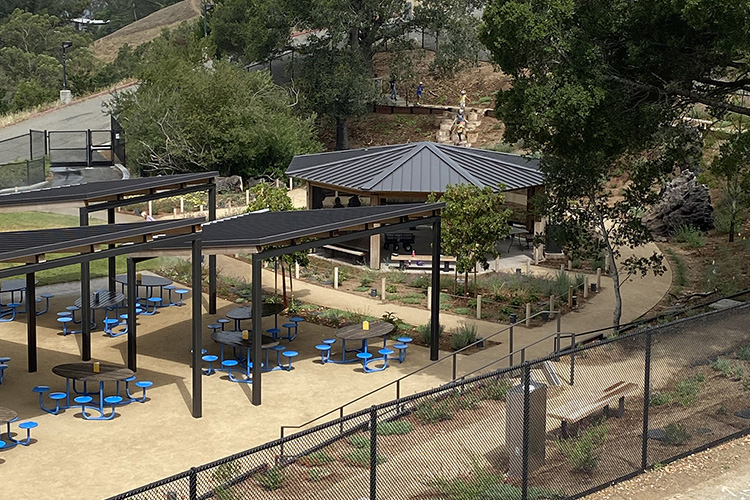 An outdoor picnic are at the new Robert and Elizabeth Karplus Outdoor Nature Lab near the Lawrence Hall of Science has bright blue seating and roofing over the top.