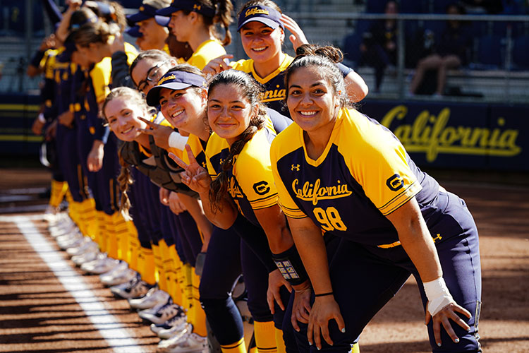 women in blue and gold pose on a softball field