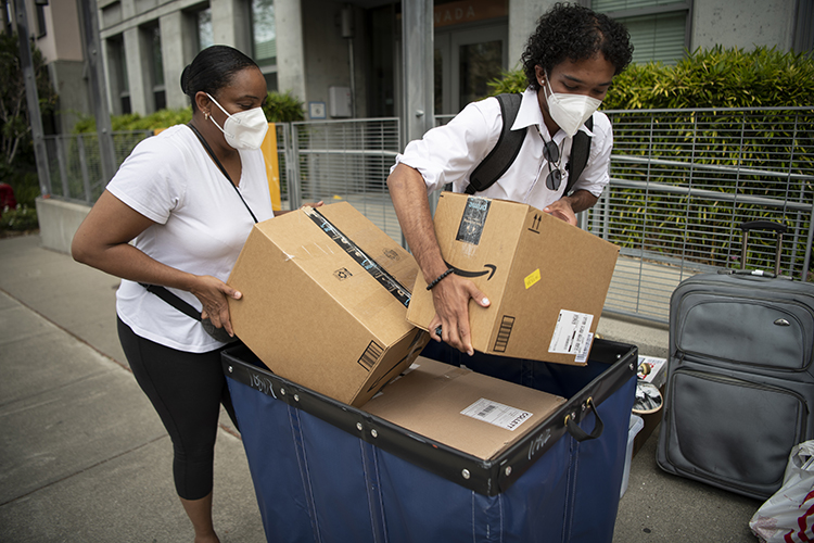 Two people who appear to be mother and son cart boxes from their vehicle down a sidewalk and into a residence hall on Move-in days 2022.