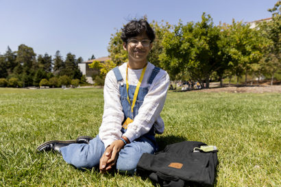 person sits on grass outside and smiles at the camera