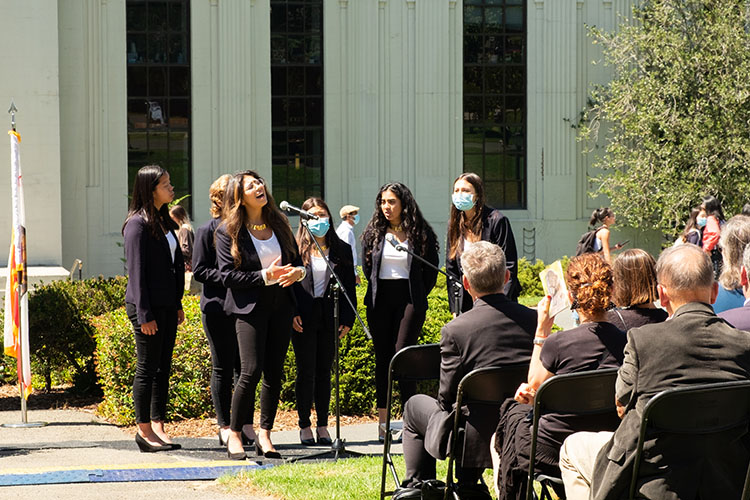 students wearing black and white stand in a circle singing around a microphone