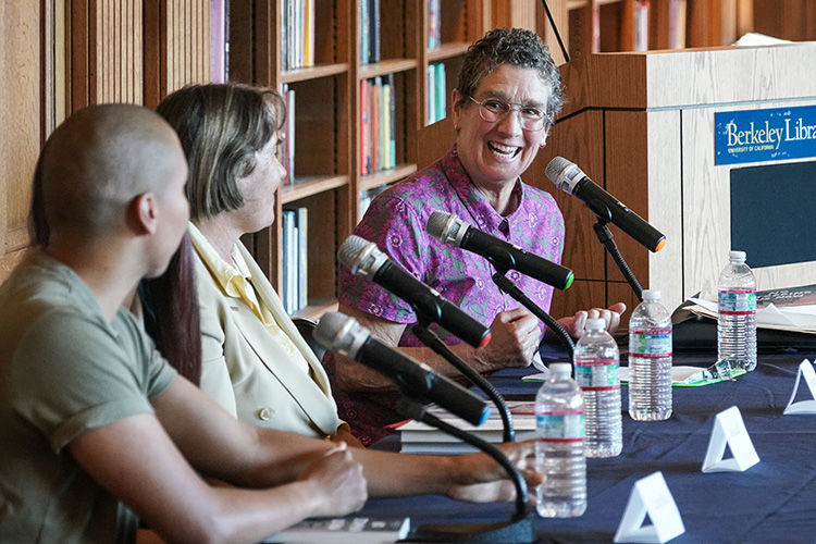 three panelists, one in a purple shirt talk at a table near a sign that says 