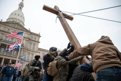 Members of right-wing extremist Proud Boys group raised a wooden cross outside the state capitol building in Lansing, Michigan, on Jan. 6, 2021. An American flag and a Trump flag are in the background.