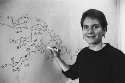 Black and white photo of a young Bertozzi writing chemical equations with a Sharpie