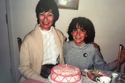 a mom and daughter smile and a cake sits on a table in front of them