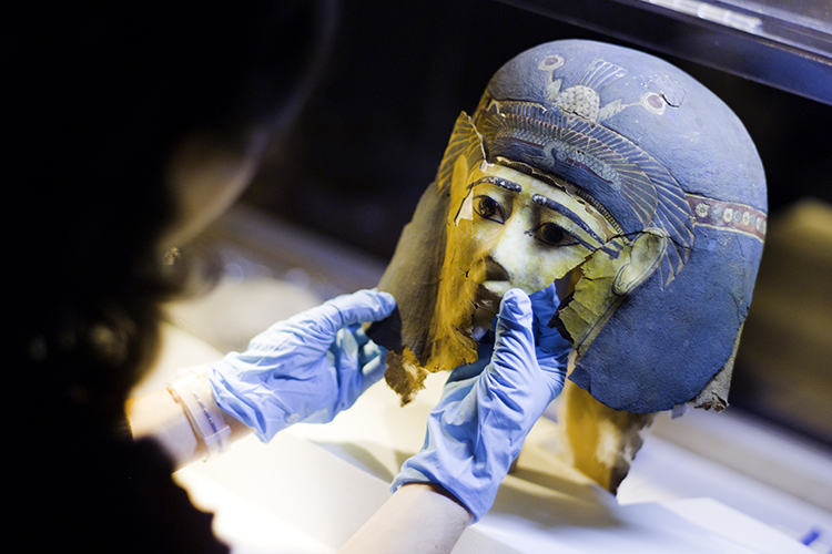 A student with rubber gloves on works on an Egyptian mask.
