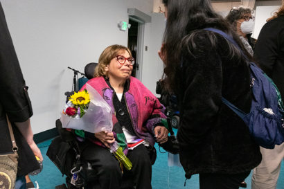 Judy Heumann talking to a student holding flowers she was given