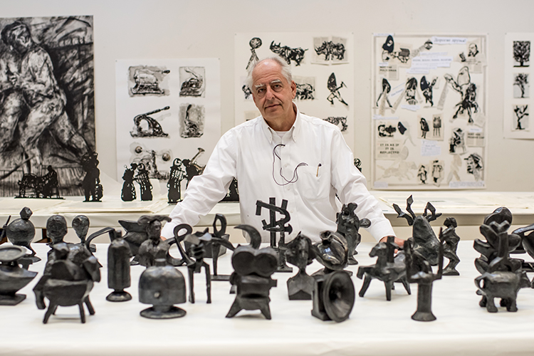 a person stands behind two dozen small metal sculptures on a table