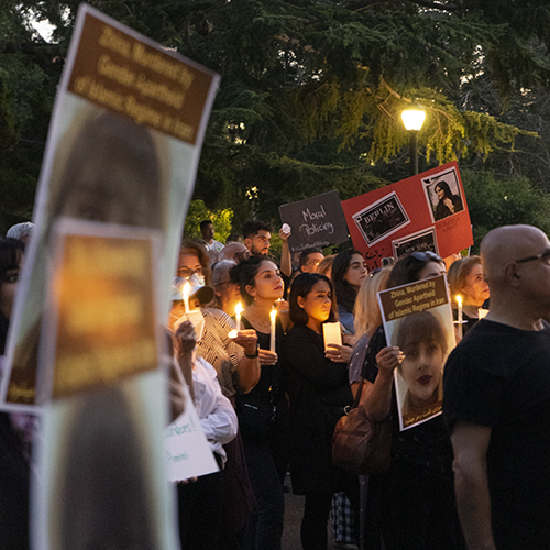 people hold candles and signs at a vigil outside at dark