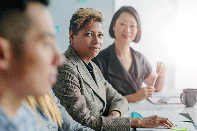 Two women in a business meeting, with a man in profile blurred in the foreground