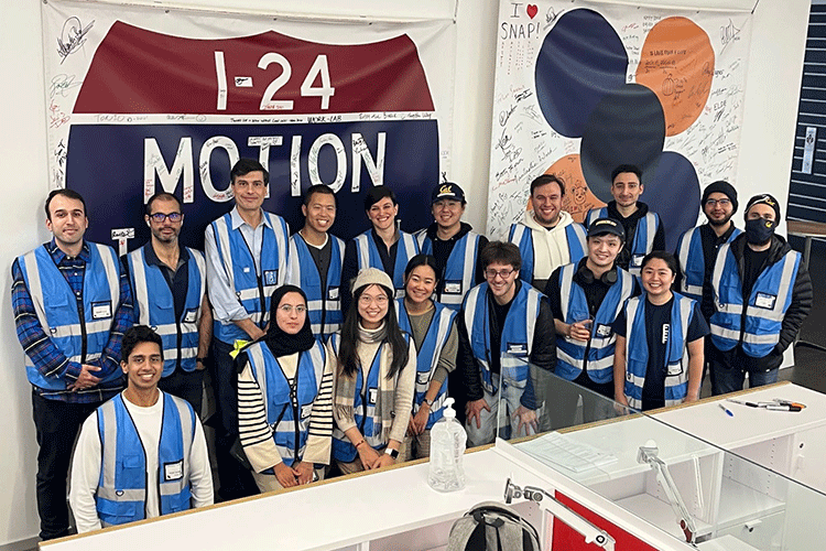 A team of researchers wearing blue safety vests poses for a group shot in front of a large sign that reads “I-24 Motion”