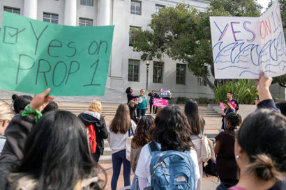 a crowd gathers on Sproul Plaza holding signs that say yes on prop 1