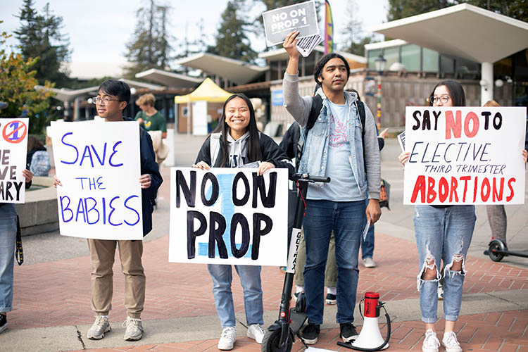 people on sproul plaza holding signs that say no on prop 1 and say no to third trimester abortions