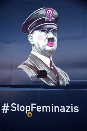 a graphic composition of Adolph Hitler in make-up over the hashtag #StopFeminazis