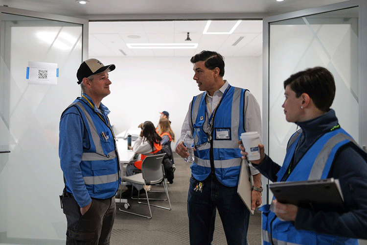 Three researchers wearing blue vests talk inside an office space