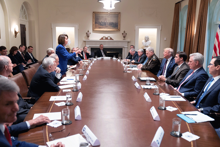 A group of nearly two dozen men sit around an oval table in the White House, as US House Speaker Nancy Pelosi, the only women visible at the table, stands and lectures President Donald Trump.