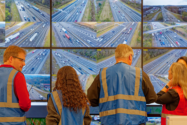 Researchers wearing blue and red vests watch monitors that display highway traffic