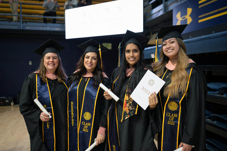 Four women wearing caps and gowns pose for a picture