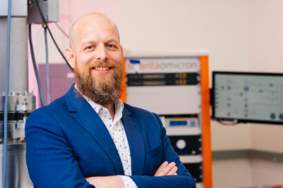 Felix Fischer with beard standing next to big microscope