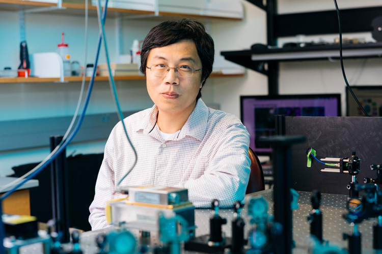 Ke Xu in his lab, with colorful optical things in the foreground