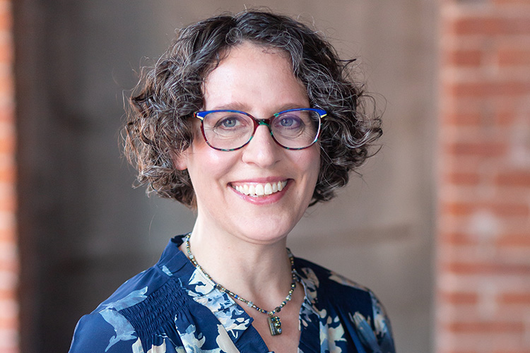 Hannah Weisman, the new executive director of The Magnes Collection of Jewish Art and Life, smiles at the camera. She is wearing eyeglasses and a print top with a necklace.