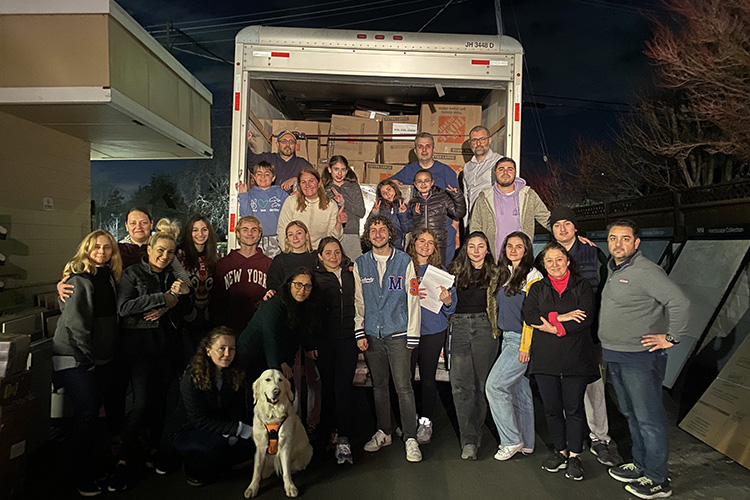 Students stand in back of a large truck with its back door open revealing boxes of items they collected to help quake victims in Turkey and Syria.