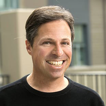 A close-up photo of Berkeley Haas distinguished teaching fellow Alan Ross. He is smiling and wearing a dark blue crew neck T-shirt.
