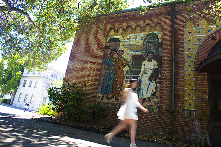 A woman in a short white dress walks past one of the mosaic murals on the Old Art Gallery building