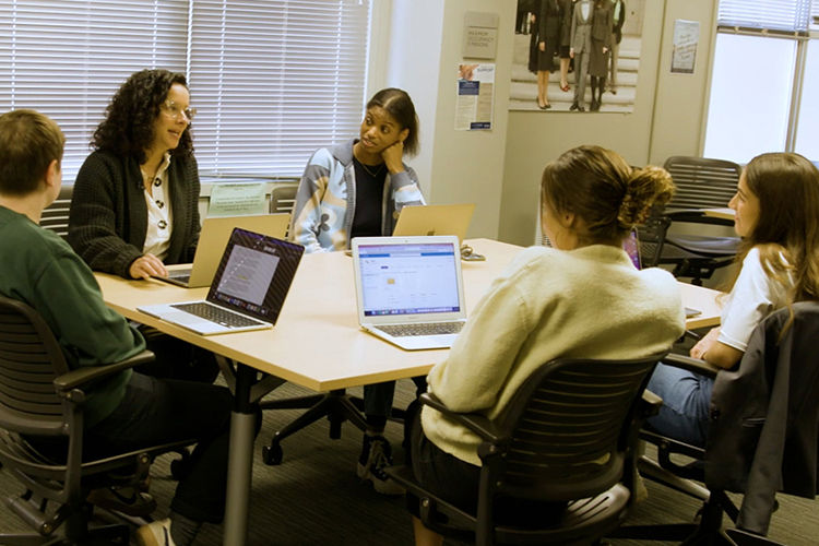 a group of people sit around a table looking at laptops