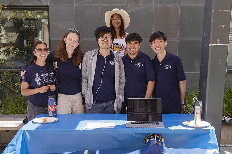 A group of five students stand behind their booth table smiling