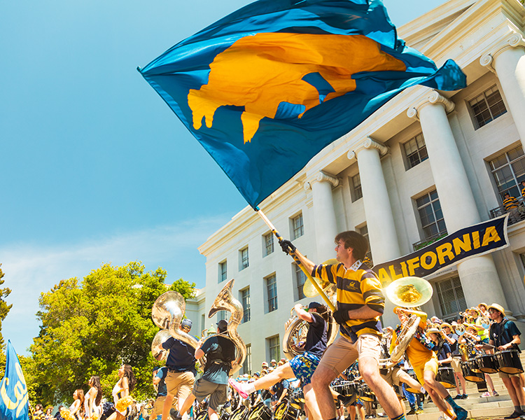 A man waves the Berkeley Bear flag on front of the Cal band on the steps of Sproul hall