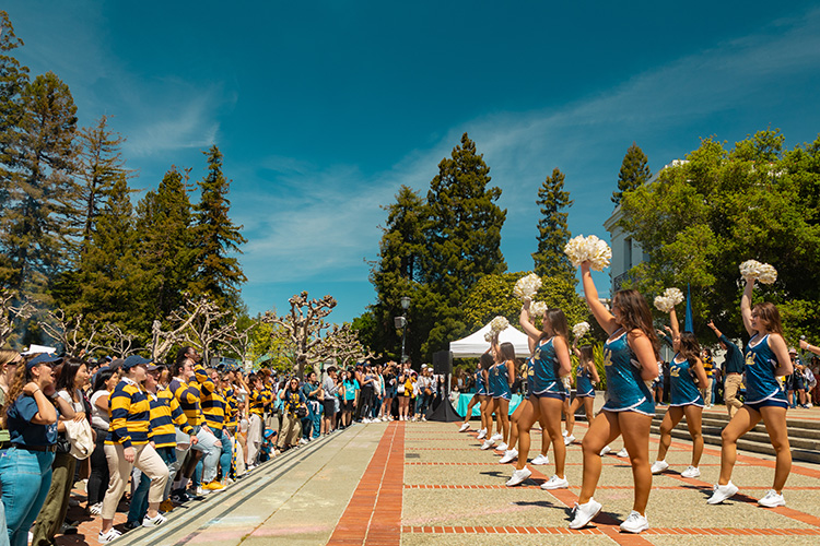 Cheerleders waving pom poms in front of Cal Day attendees.