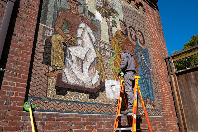 A worker on a ladder starts restoration work on the mosaic mural.