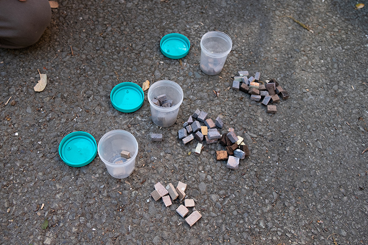 Containers and individual colorful tiles rest on the ground near where restoration of the Old Art Gallery building's mosaics are being restored