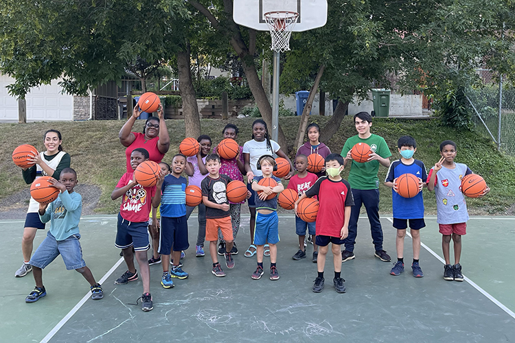 a dozen kids and three adults hold basketballs on a court